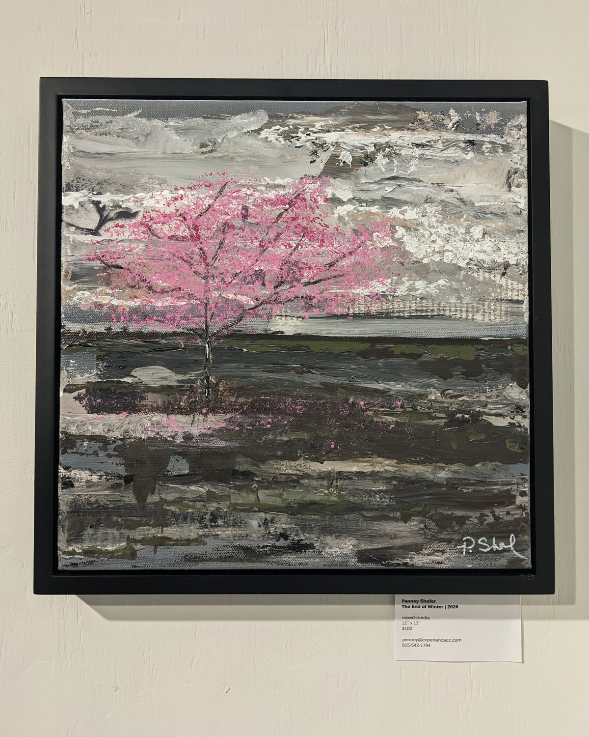 A framed abstract landscape painting featuring a prominent pink tree against a textured gray and white background, hung on a beige wall with a small label card below it.