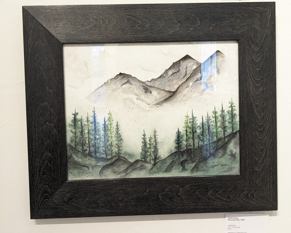 A framed landscape artwork featuring a mountain scene with pine trees, displayed on a white wall.