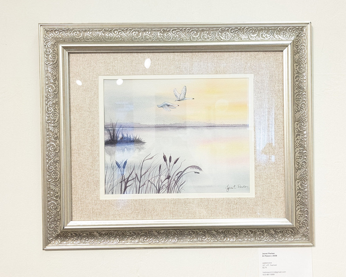 Framed artwork of two birds flying over a pond with the sun in the background.