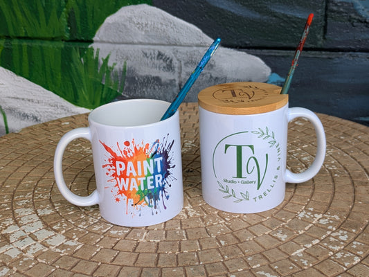 Two mugs on a stone surface with a colorful paintbrush design and a logo.